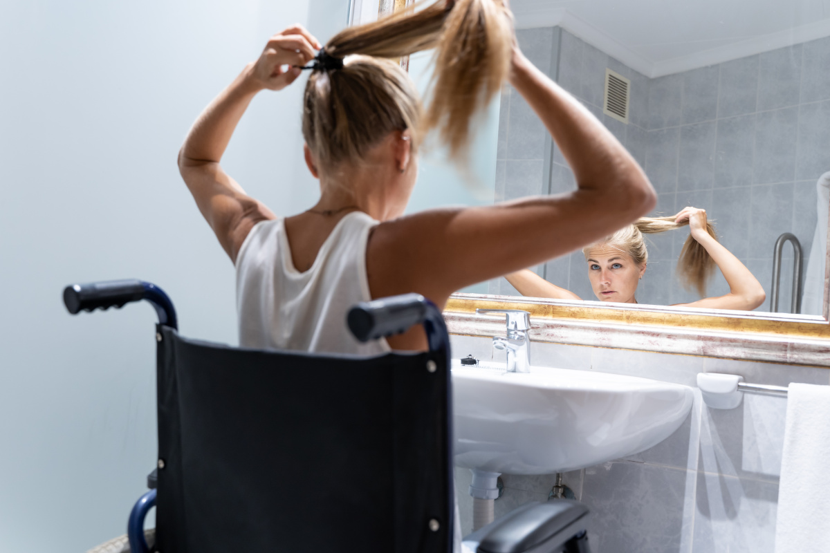 Accessible walk-in shower room in Winchester featuring wheelchair-adapted wash basin with young woman brushing hair.